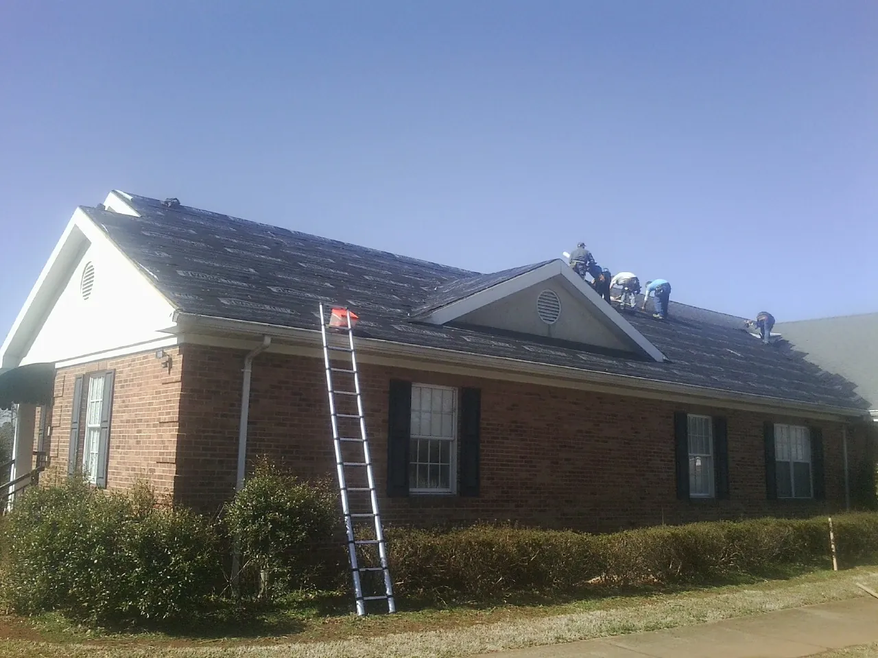Crew tearing shingles off a brick ranch roof with a ladder set — Emergency Roof Repair work by our crew in Hickman
