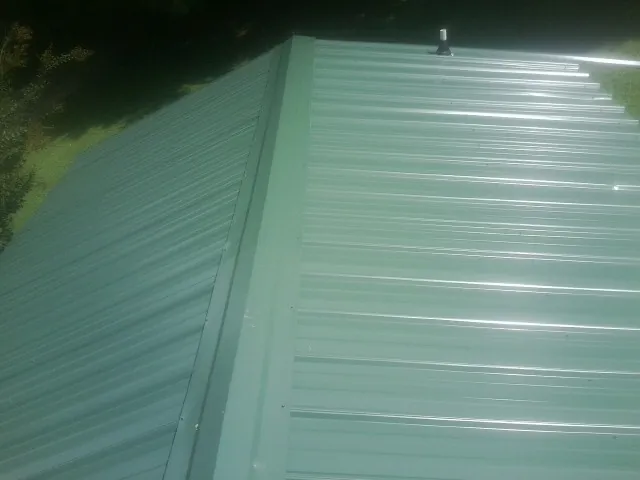 New green metal panels meeting at the ridge of a roof — Flat Roof Repair work by our crew in Hickman