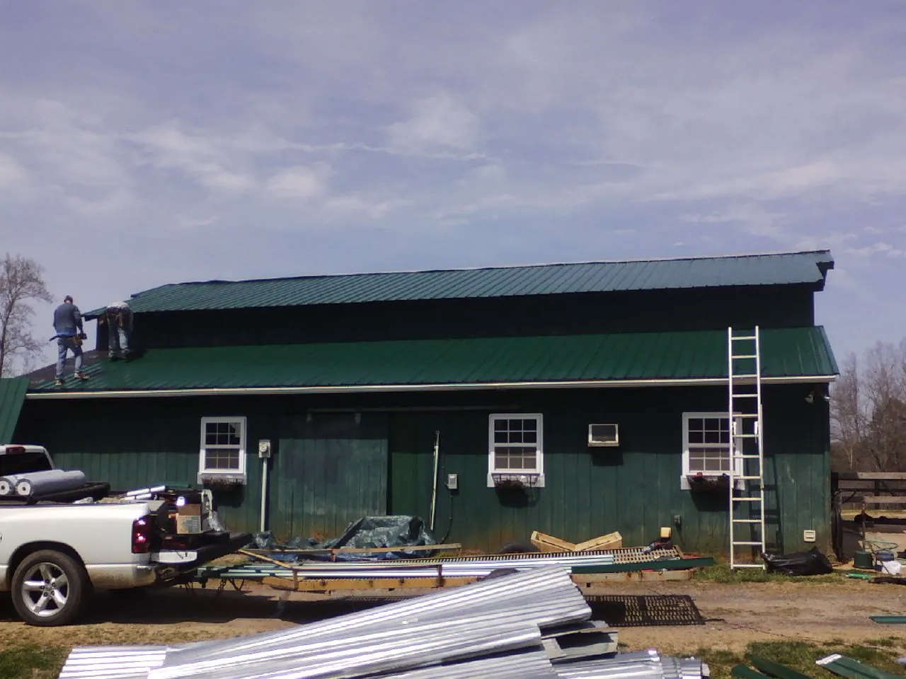 Crew installing green metal roofing on a large green barn in Hickman